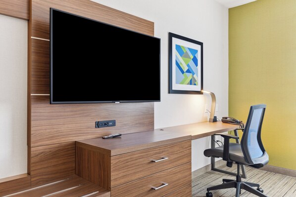 Una habitación de hotel moderna con un escritorio de madera, un televisor de pantalla plana, un cuadro abstracto enmarco y una silla de oficina negra.