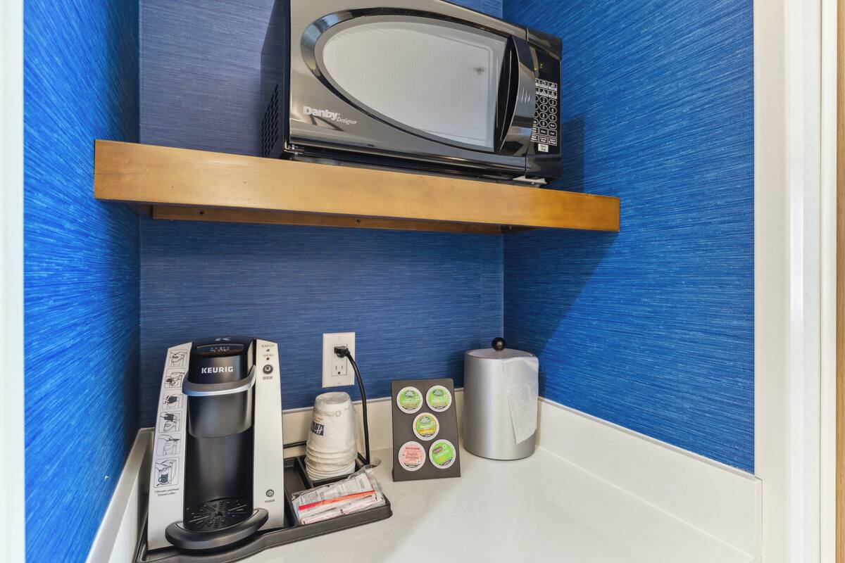 Una kitchenette con microondas, cafetera y cápsulas de café.