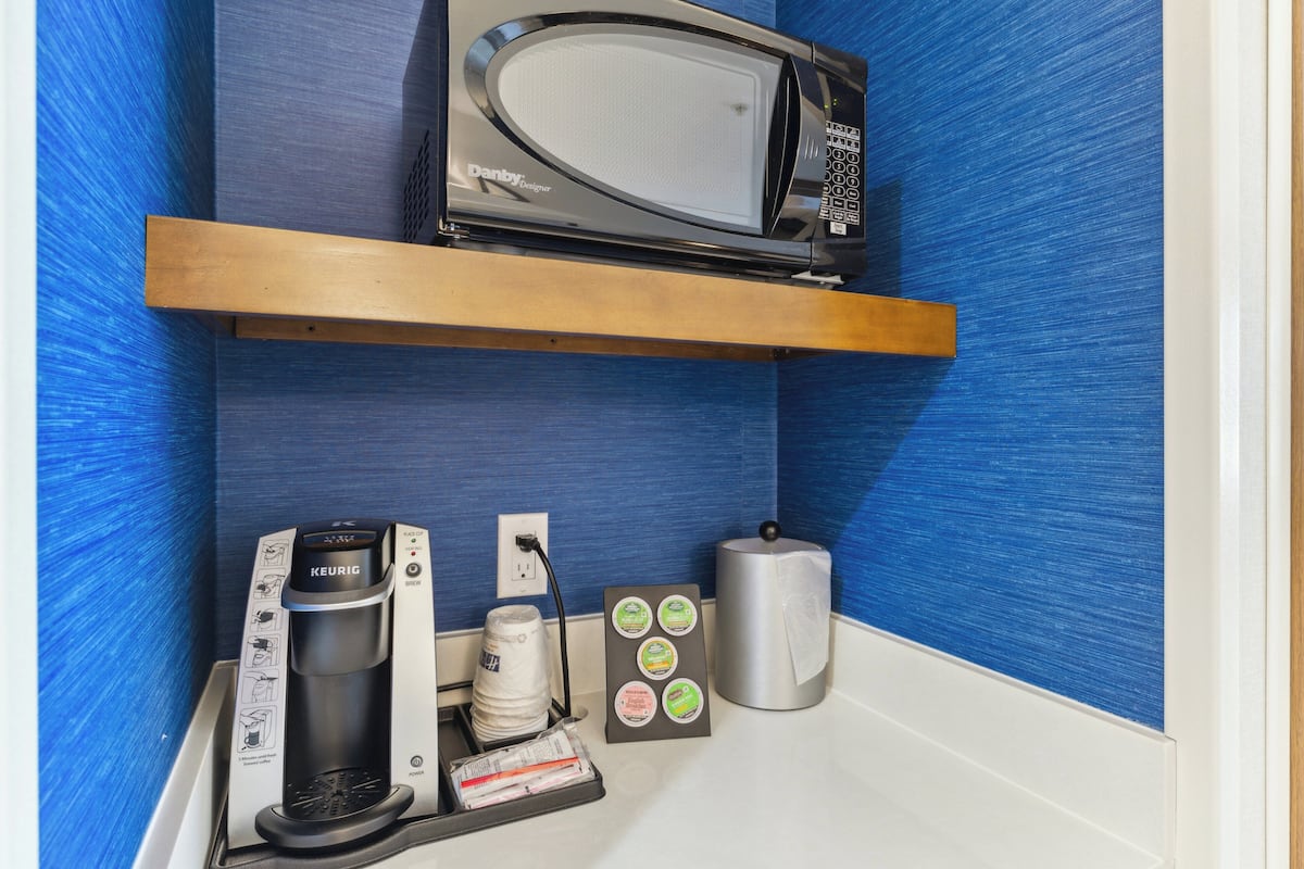 Una kitchenette con microondas, cafetera y cápsulas de café.
