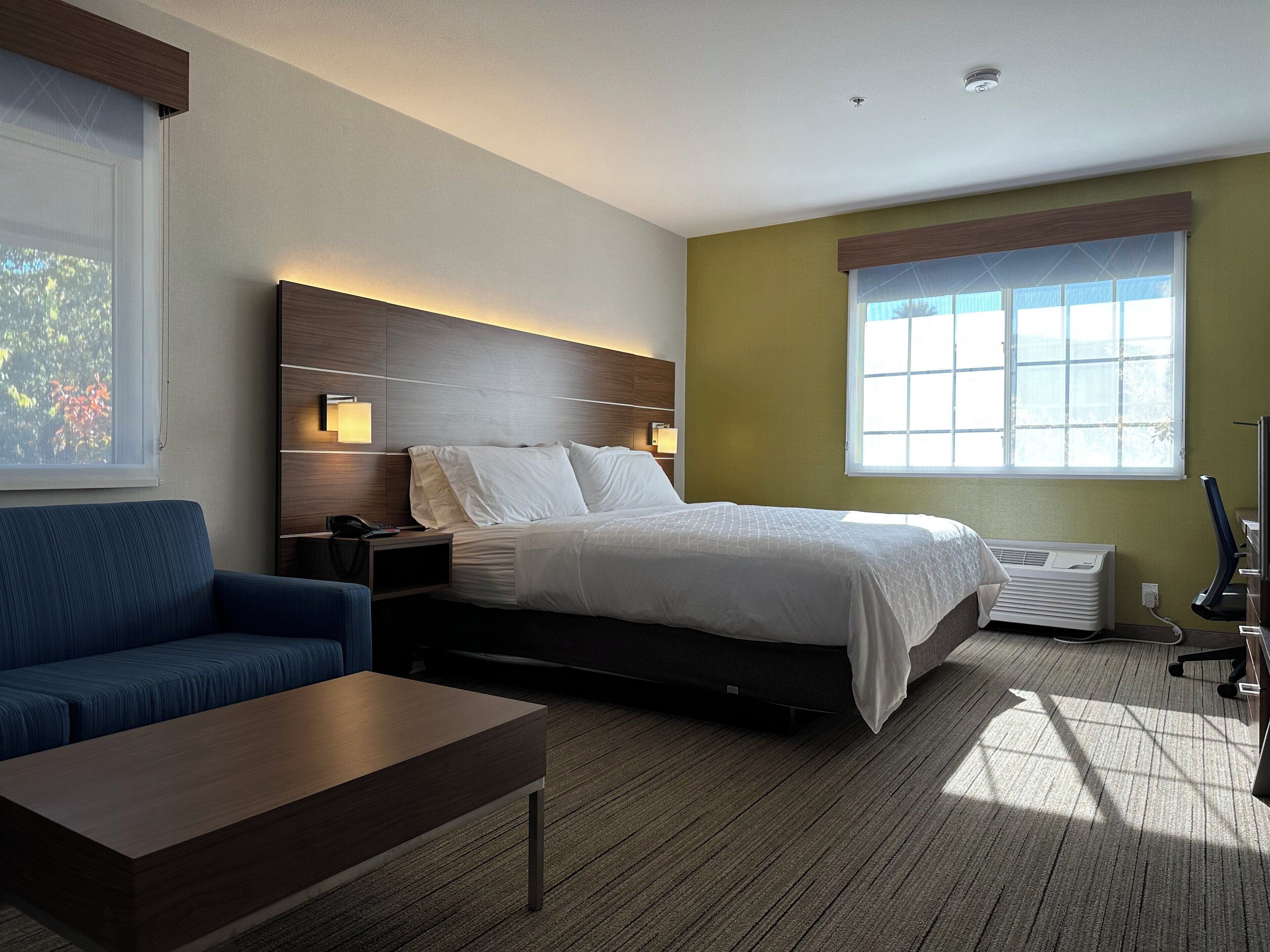 A modern hotel room with a bed, a sofa, a desk, and a large window.