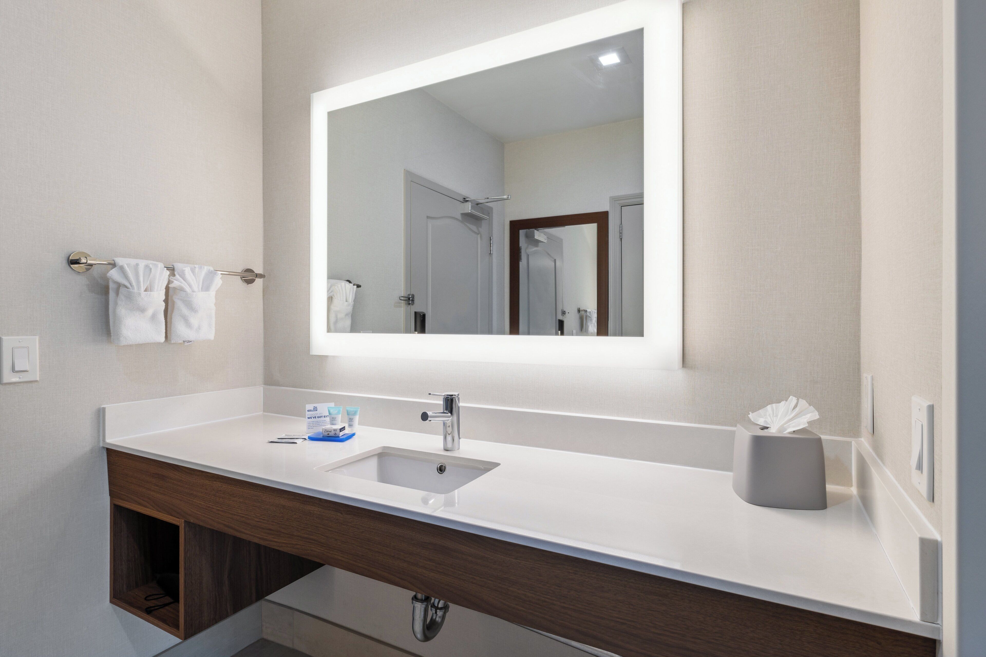 Un baño moderno con un lavabo blanco, un espejo grande y un perchero para toallas.