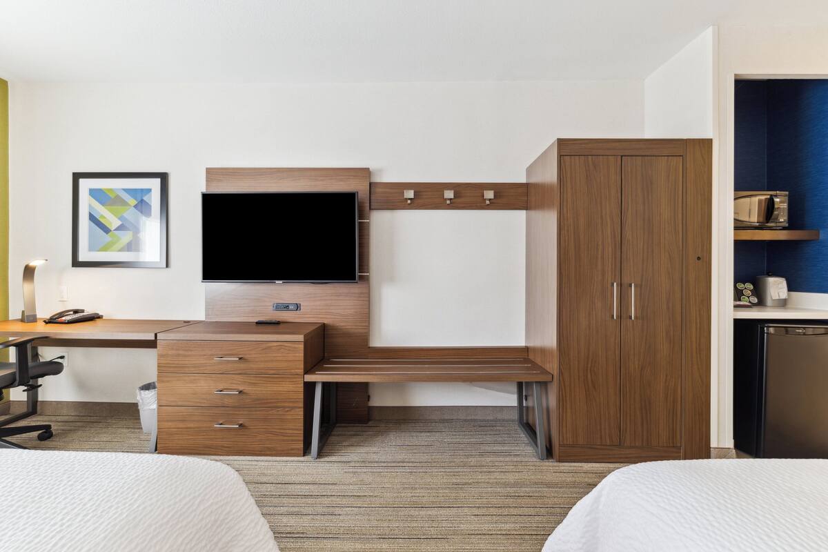 Habitación de hotel con escritorio de madera, televisor de pantalla plana, armario y kitchenette.