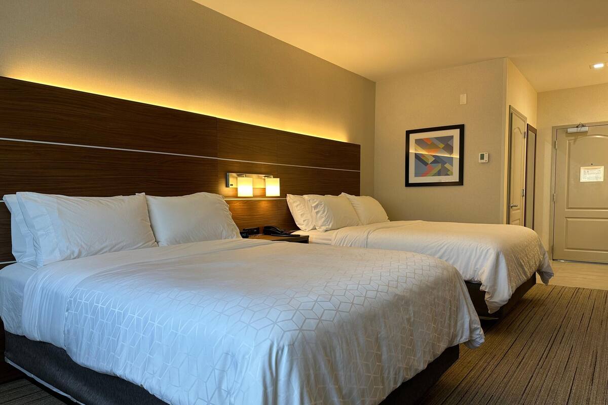 A hotel room with two beds, a headboard, bedside lamps, a framed picture, and a door.