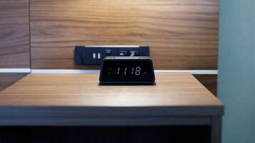 A digital clock on a wooden table in a room with a wooden panel wall.
