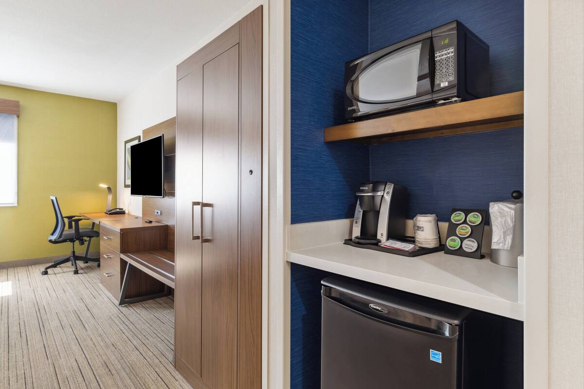 Una habitación de hotel con kitchenette, televisión de pantalla plana, escritorio y silla.