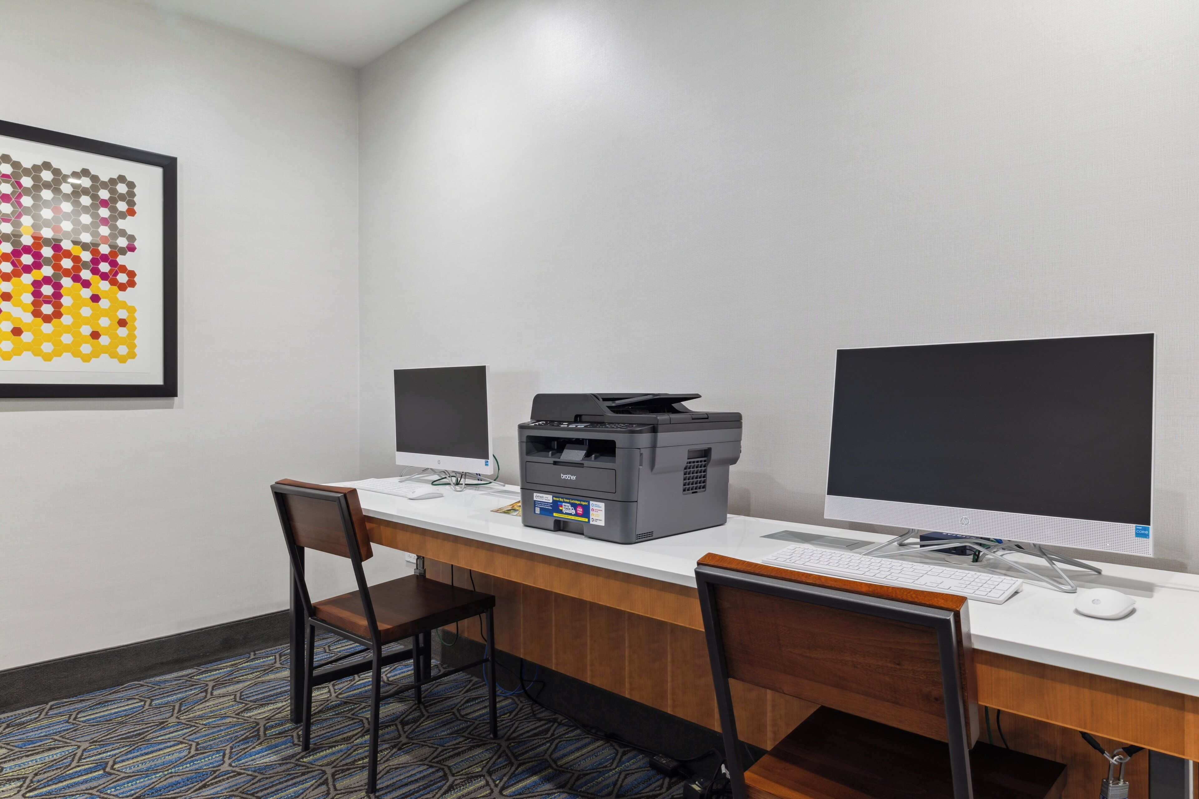 A workspace with two monitors, a printer, and a keyboard on a white desk.