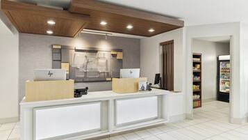A reception area with a modern design, featuring a reception desk, a mirror, and a wall-mounted display.