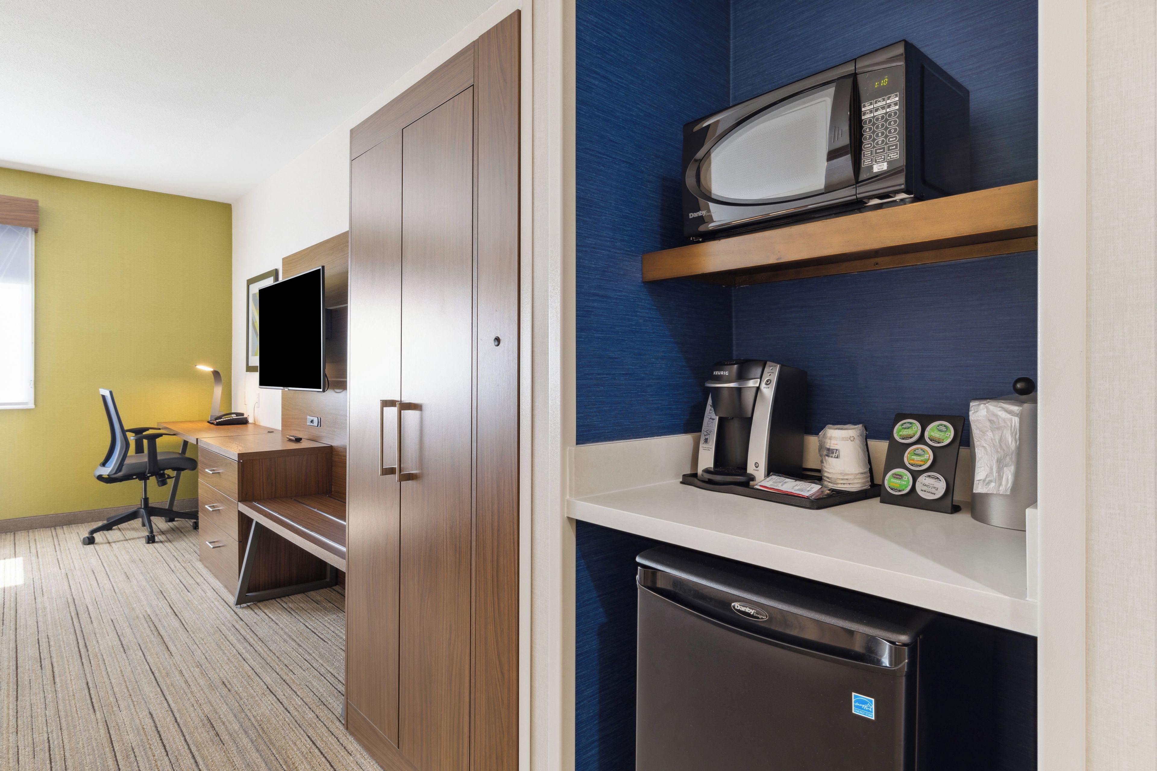 A hotel room with a kitchenette, a microwave, a coffee machine, and a refrigerator.