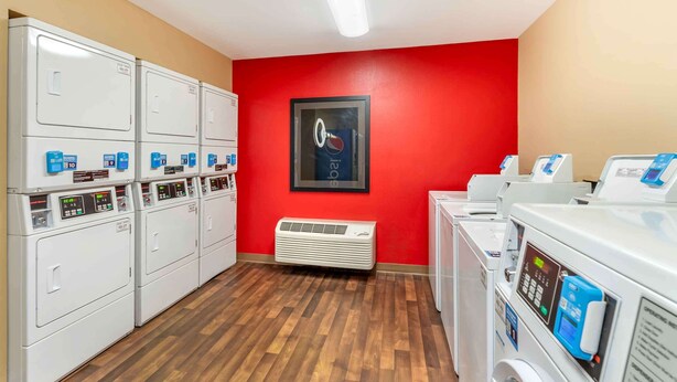 Un cuarto de lavandería con varias lavadoras y secadoras, una pared roja y un cuadro enmarcado.