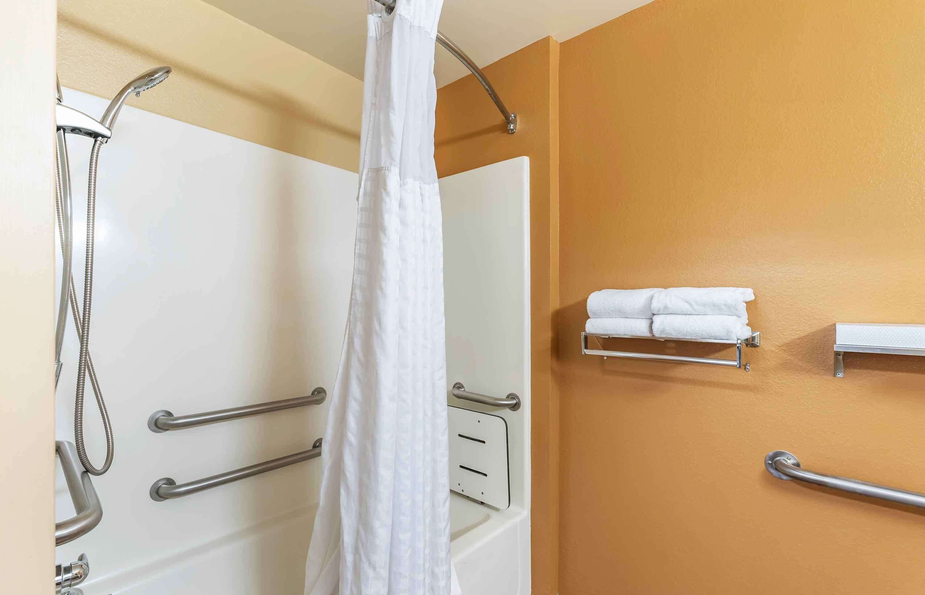 A bathroom with a shower, grab bars, a towel rack, and a wall-mounted towel dispenser.