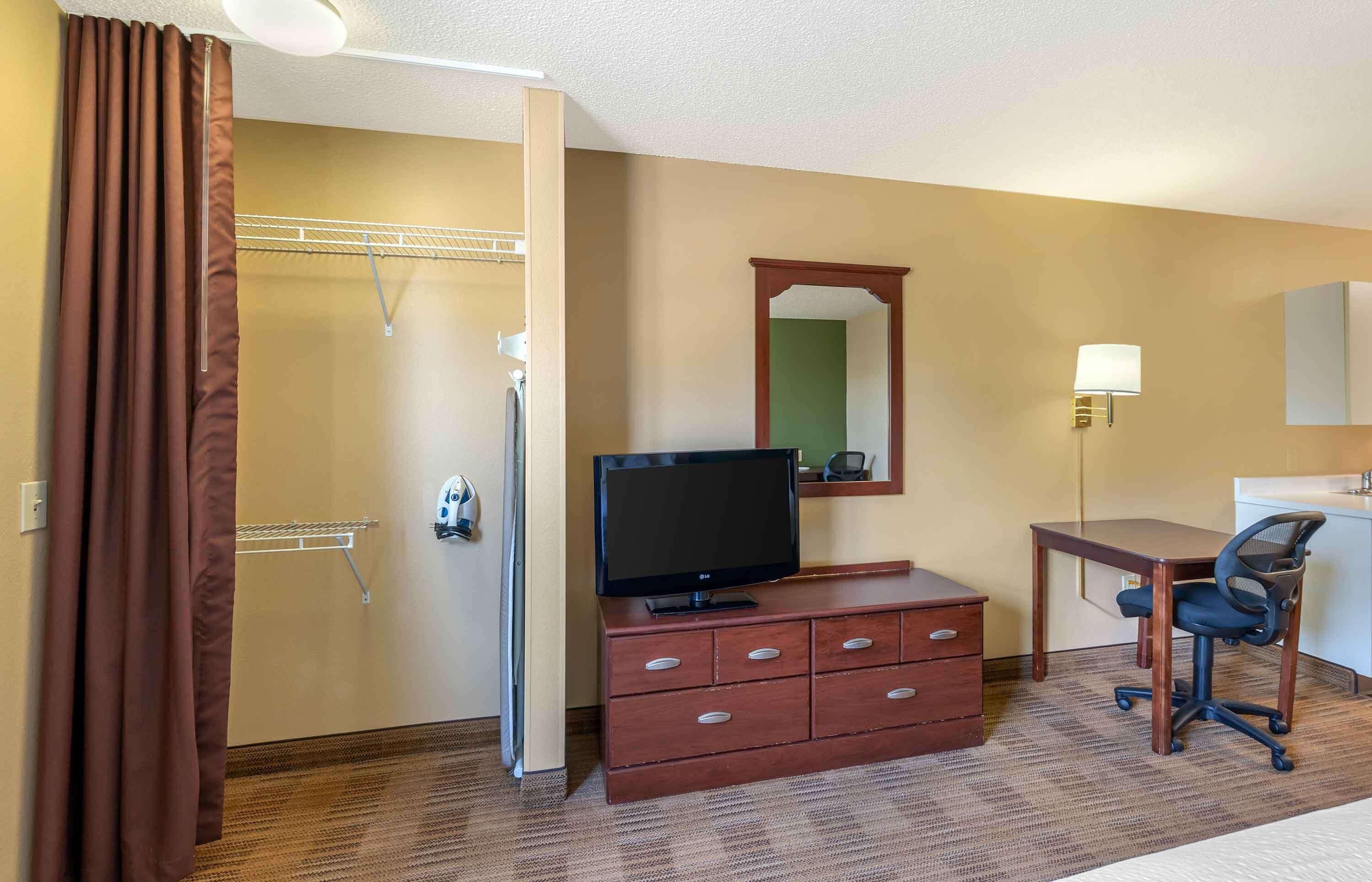 Habitación de hotel con ducha, un televisor sobre un aparador de madera, un escritorio con silla y un espejo en la pared.