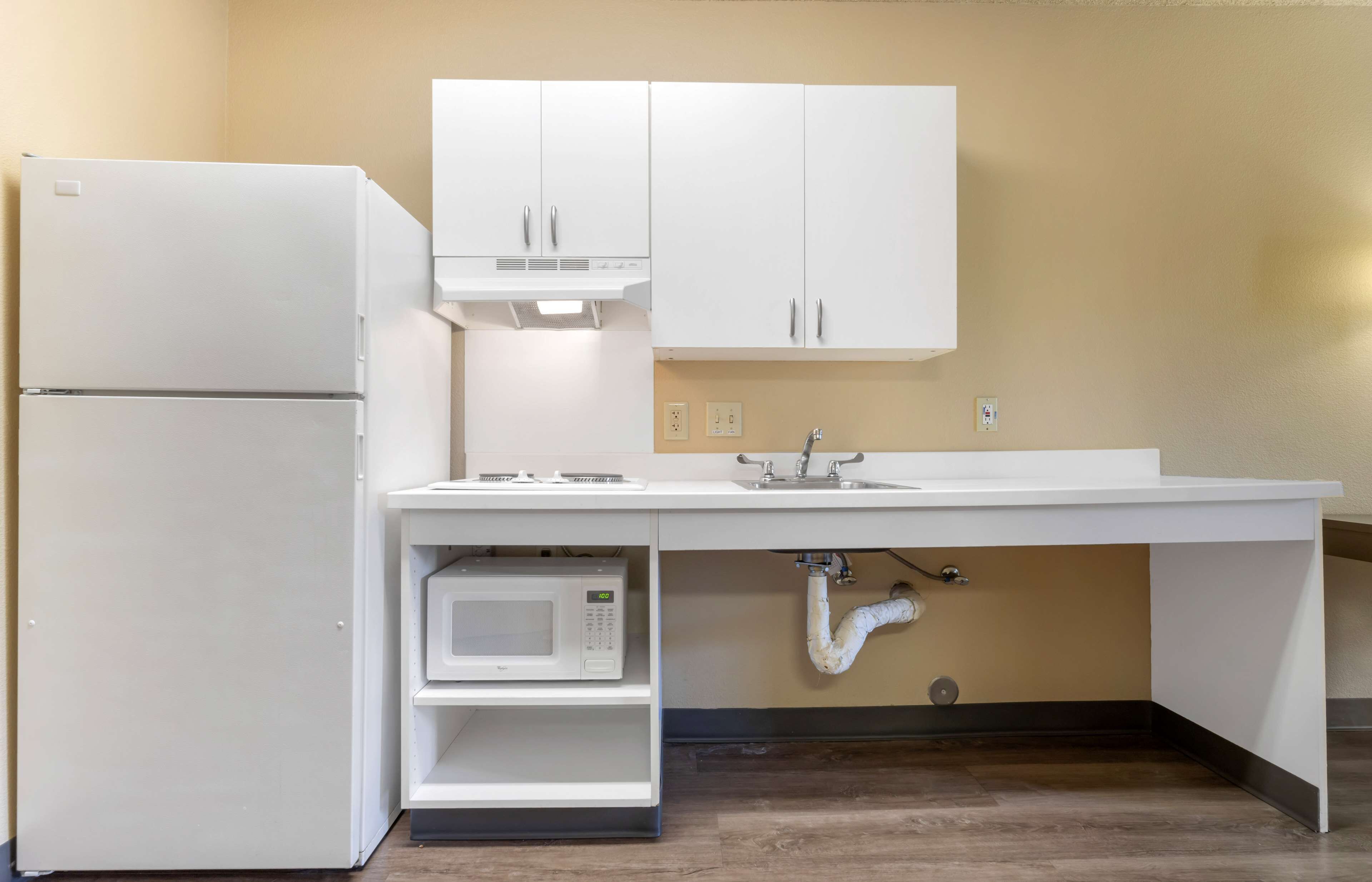 A compact kitchen with white cabinets, a built-in microwave, and a sink under a countertop.