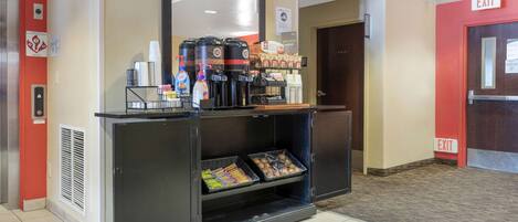 Zona de recepción de hotel con estación de café, un cubo de basura y señal de salida.