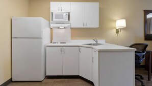 Une cuisine de taille réduite, avec des meubles blancs, un four à micro-ondes, un réfrigérateur, un évier et une chaise.