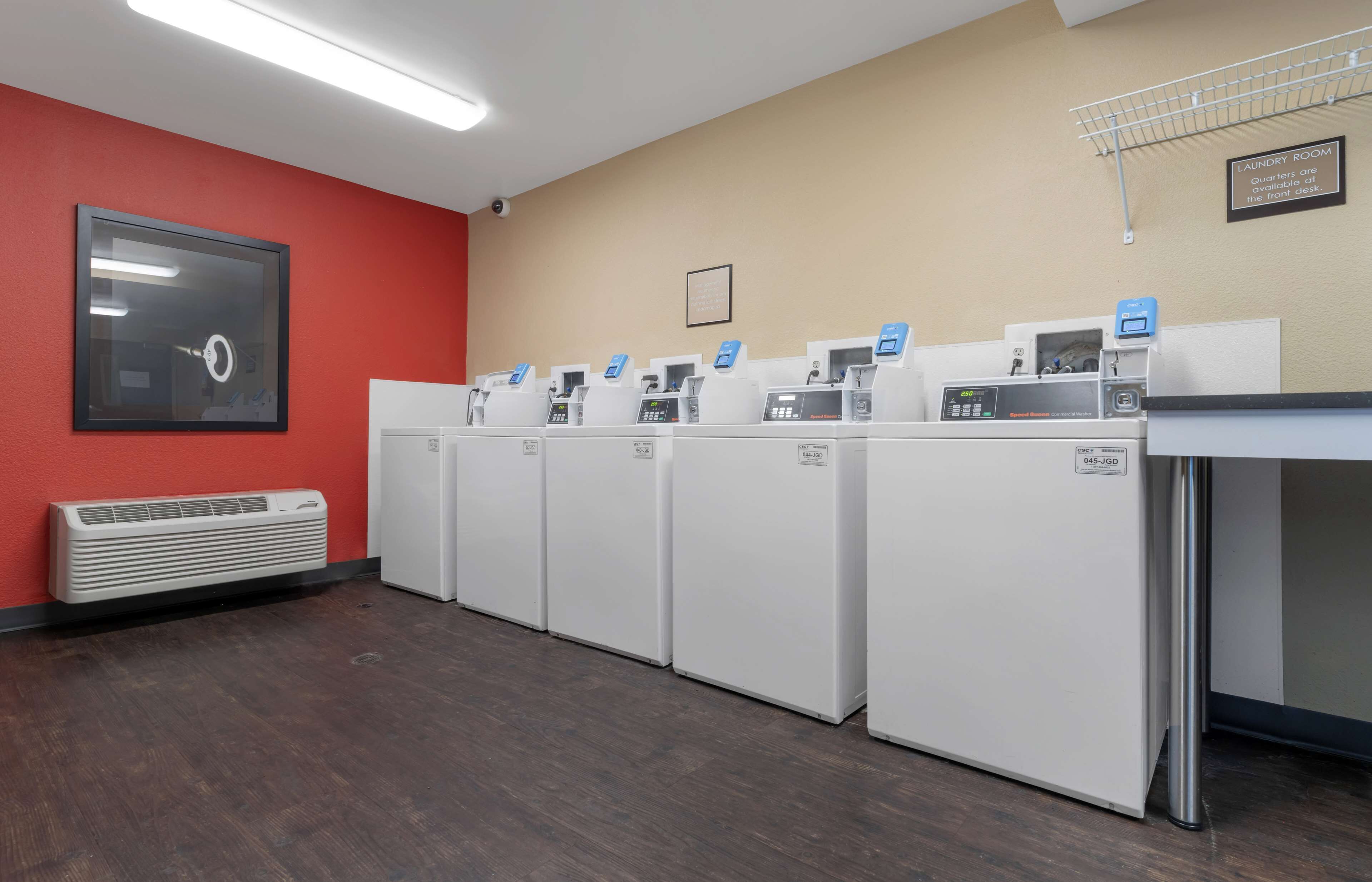 A laundry room with multiple washing machines and dryers, a red wall, and a ceiling-mounted air conditioning unit.