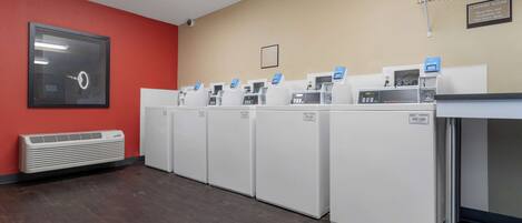 A laundry room with multiple washing machines and dryers, a red wall, and a ceiling-mounted air conditioning unit.