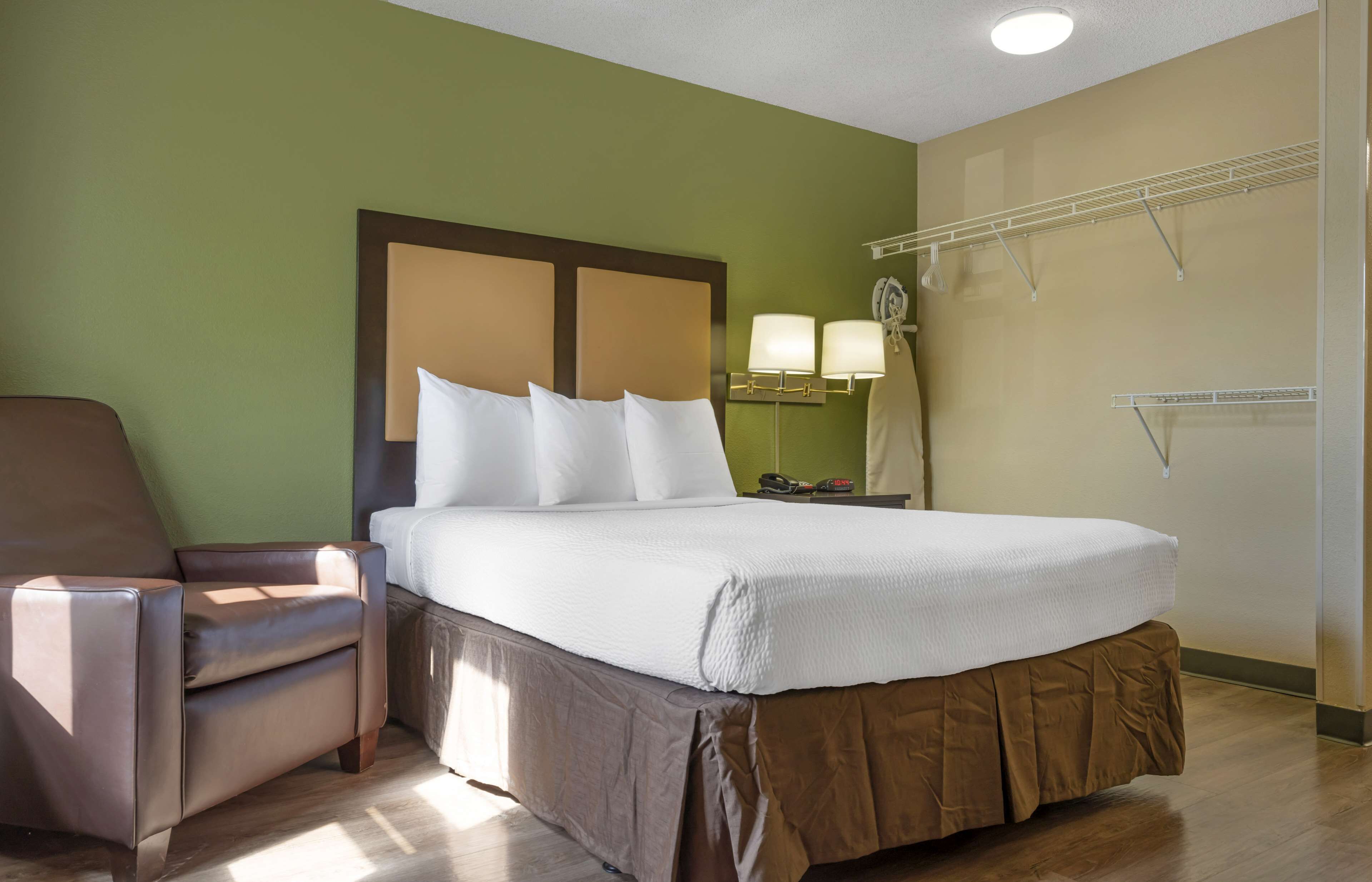 A hotel room with a large bed, a chair, a nightstand, a lamp, and a wardrobe.