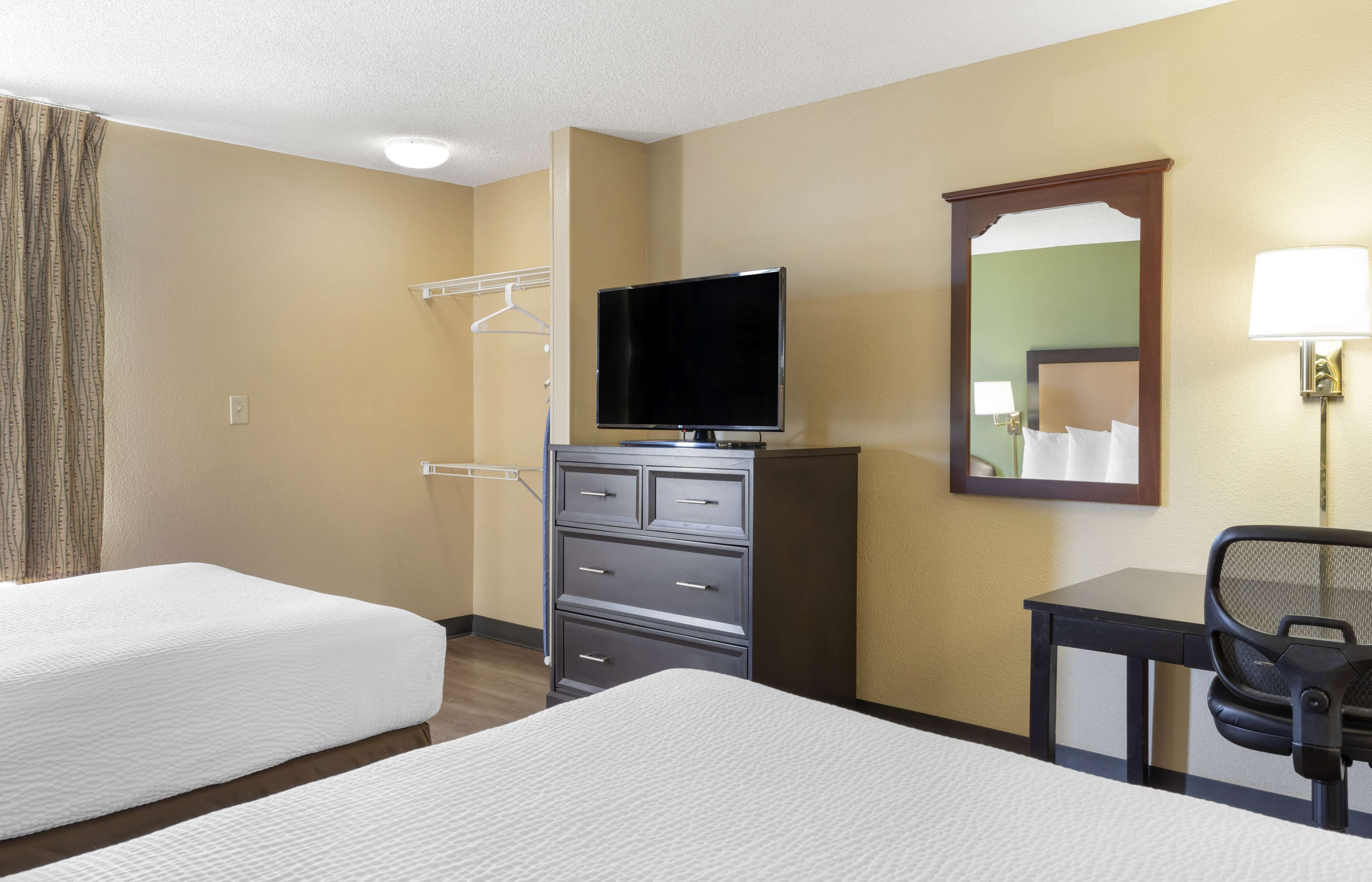 Une chambre d’hôtel avec deux lits, une télévision, un bureau avec une chaise, un miroir et une lampe.