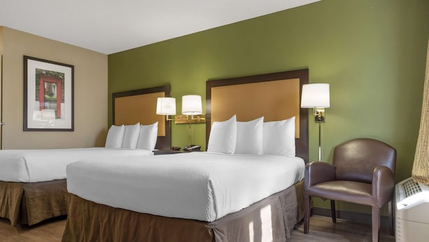 Une chambre d’hôtel avec deux lits, une chaise et un bureau avec une lampe.