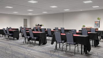 Un salón de conferencias con filas de mesas y sillas, suelo alfombrado y una pizarra.