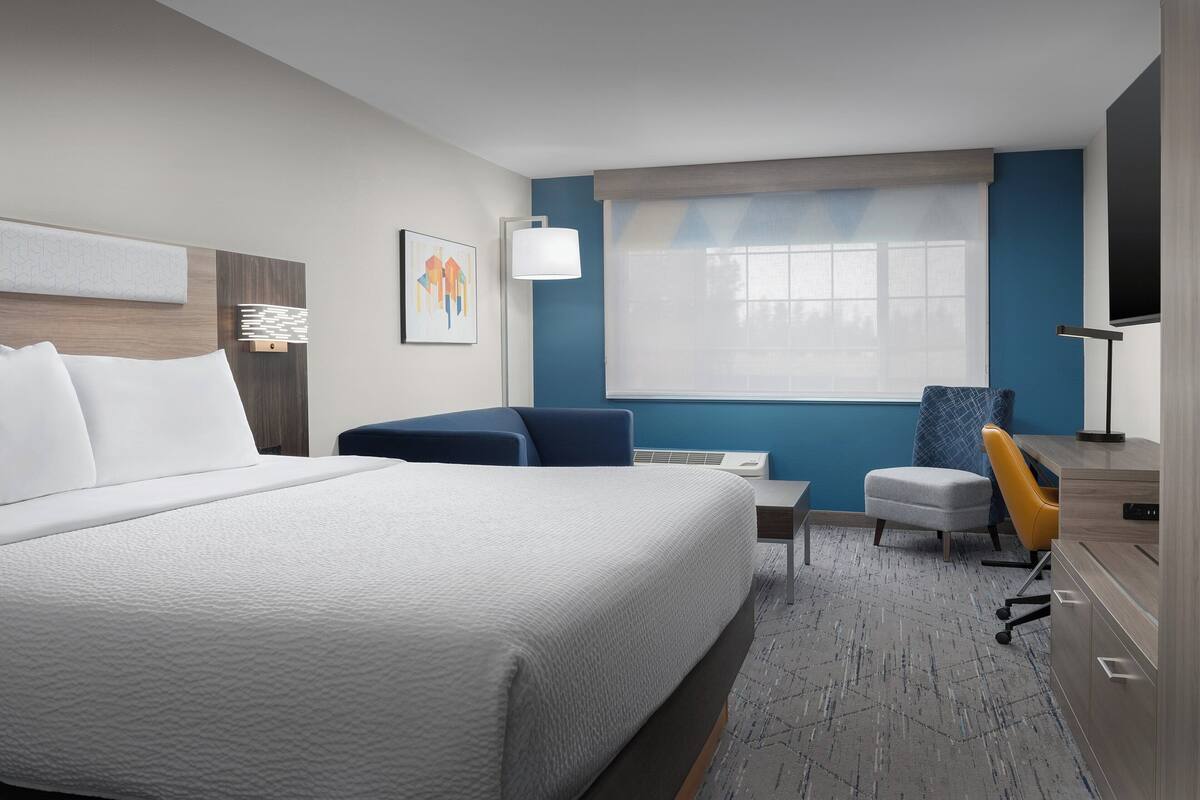 A hotel room with a large bed, a desk, a chair, and a TV.