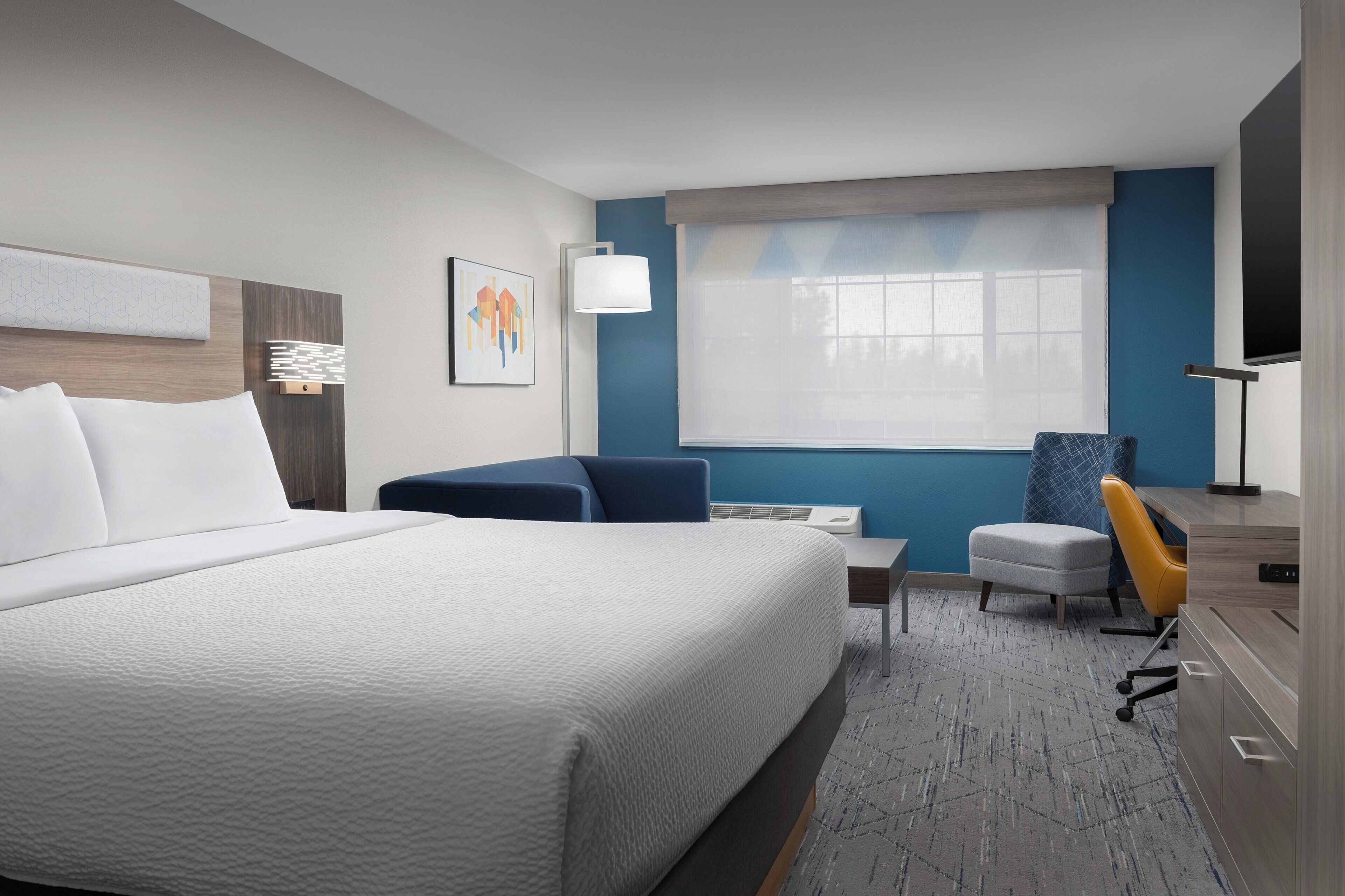 A hotel room with a large bed, a desk, a chair, and a TV.
