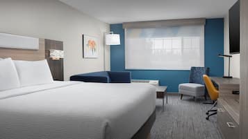 A hotel room with a large bed, a desk, a chair, and a TV.