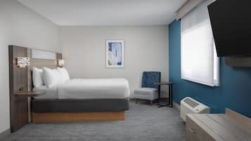 A modern hotel room with a bed, a small seating area, a TV, and a window.