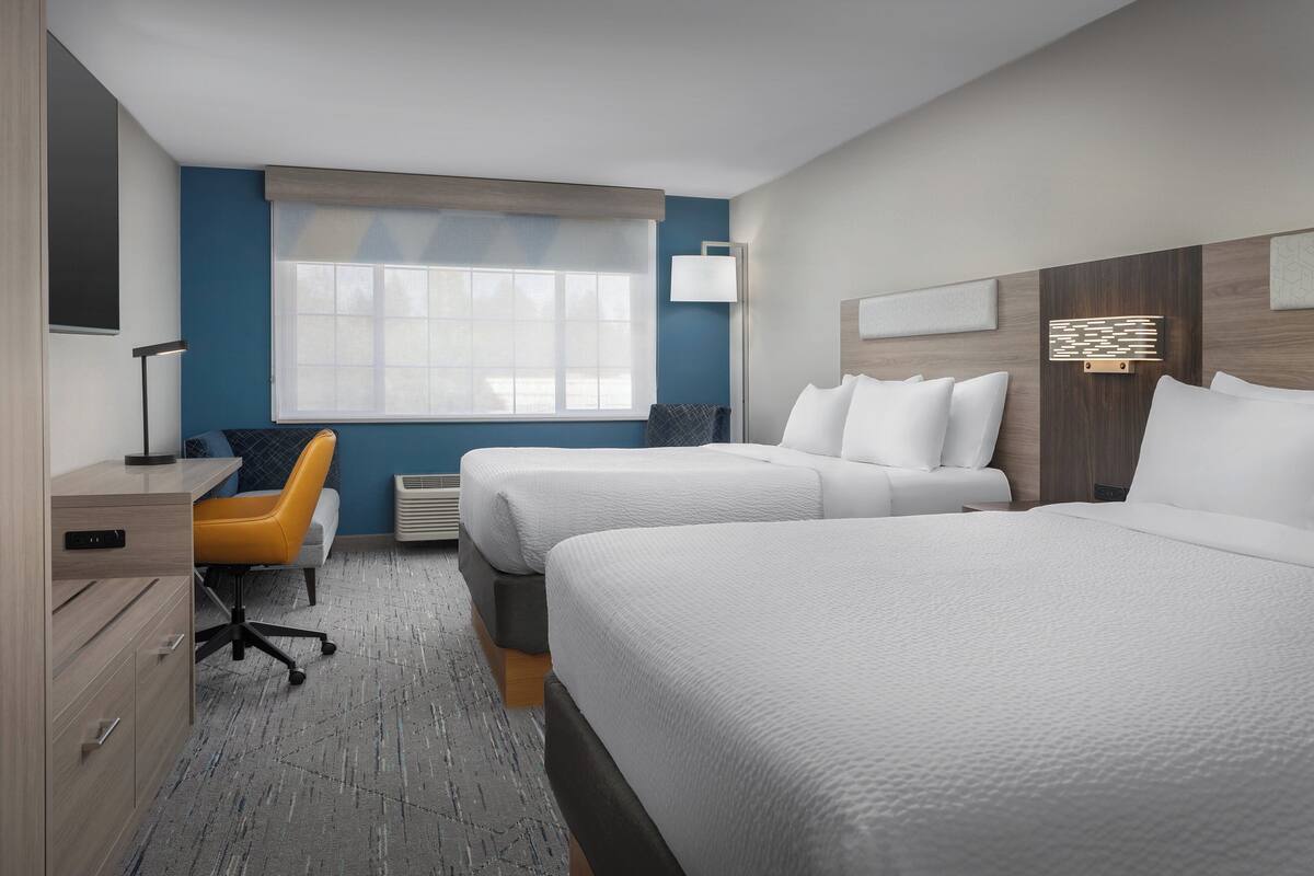 A hotel room with two beds, a desk, a chair, and a window with blinds.
