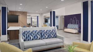 A modern lobby with a grey sofa, yellow armchairs, a flat-screen TV, and a cityscape mural. - Holiday Inn Express Spokane Airport by IHG (Spokane)