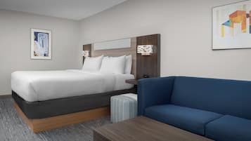 A modern hotel room with a bed, a blue sofa, a wooden coffee table, and two wall-mounted lamps.