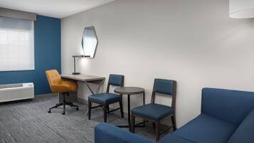 Quarto de hotel com parede azul, uma escrivaninha com cadeira, um sofá e uma mesa pequena.
