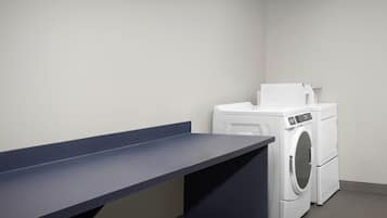 Un lavadero con lavadora y secadora, un banco azul oscuro y una pared blanca.