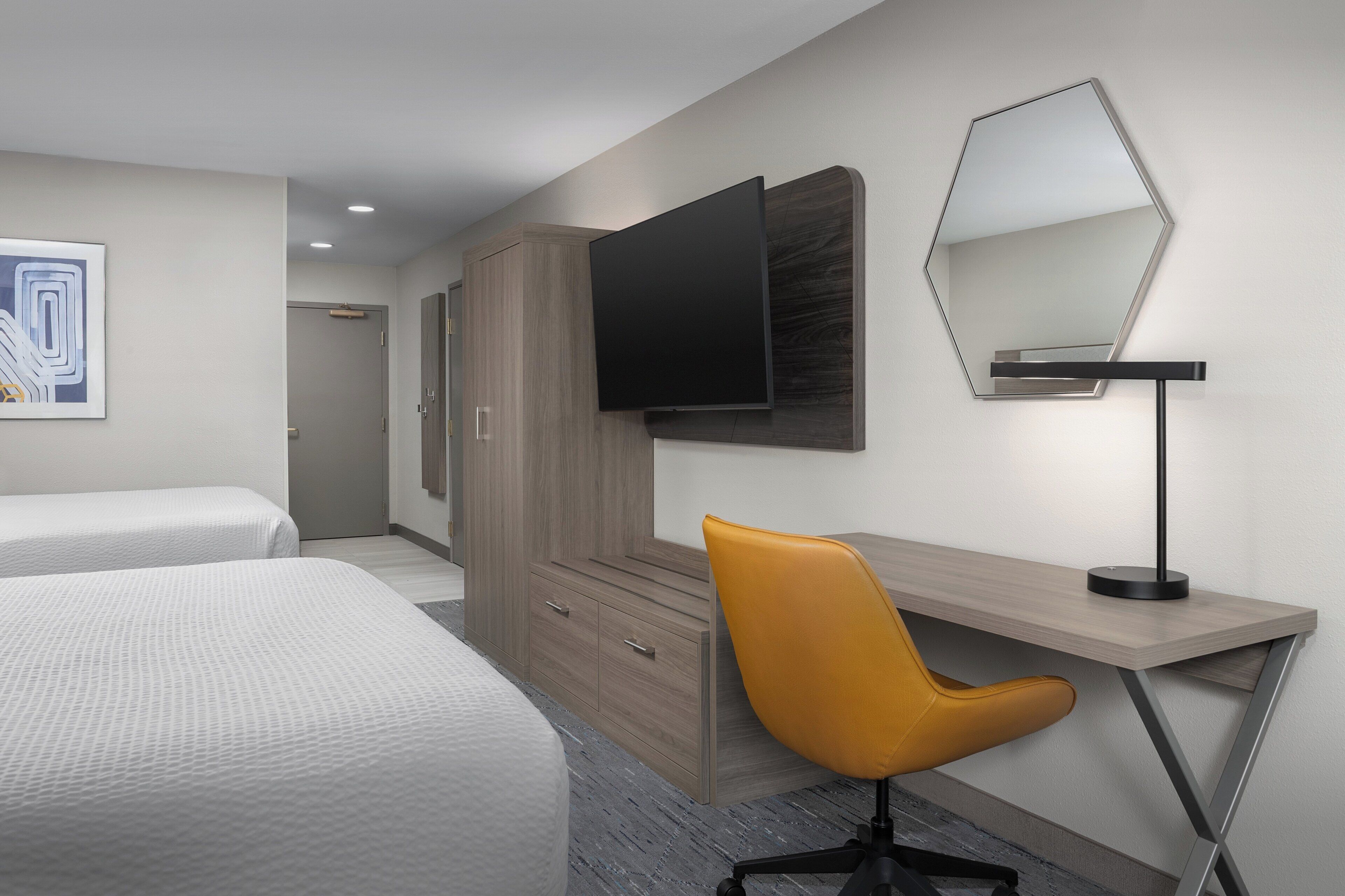 Une chambre d’hôtel avec deux lits, un bureau, une chaise, un téléviseur à écran plat et un miroir.