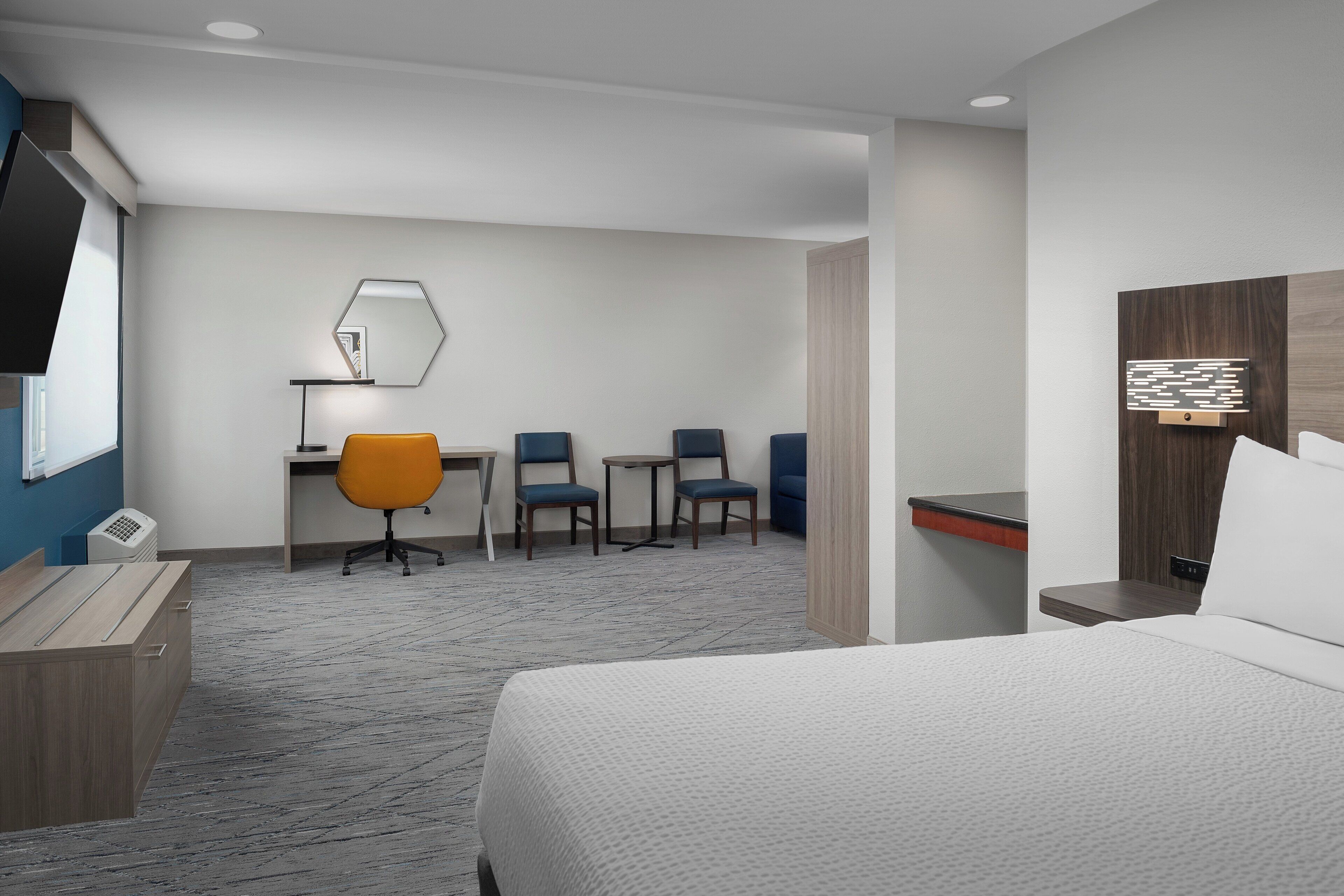 Et hotelværelse med en seng, et skrivebord med to stole, et lille bord og et fjernsyn.
