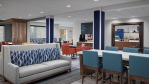 A modern hotel lobby with a grey sofa, orange chairs, a long table, and a coffee station. - Holiday Inn Express Spokane Airport by IHG (Spokane)