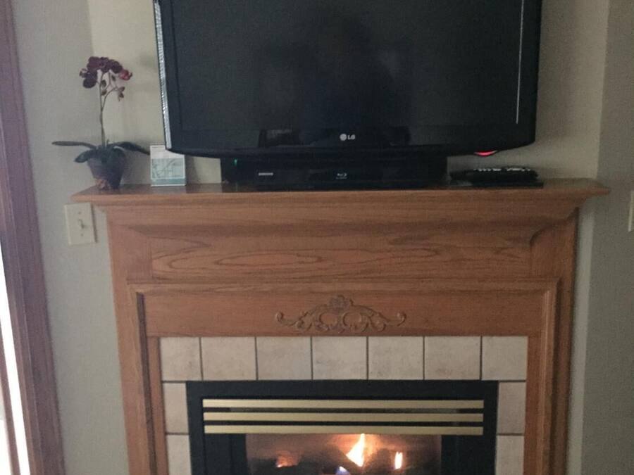 A living room with a flat-screen TV mounted on a wooden mantel above a tiled fireplace.