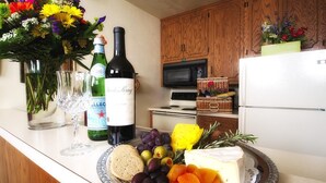 A kitchen counter with a plate of cheese, grapes, and dried fruits, a bottle of wine, and a vase of flowers.