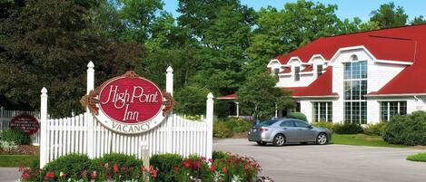 A hotel sign with a red and white design, a white picket fence, and a car parked in front.