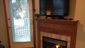 A living room with a fireplace, a television mounted above it, and a door with a view to the outside.