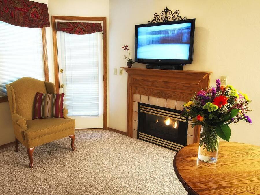 A living room with a beige armchair, a fireplace, a television, and a vase of flowers.
