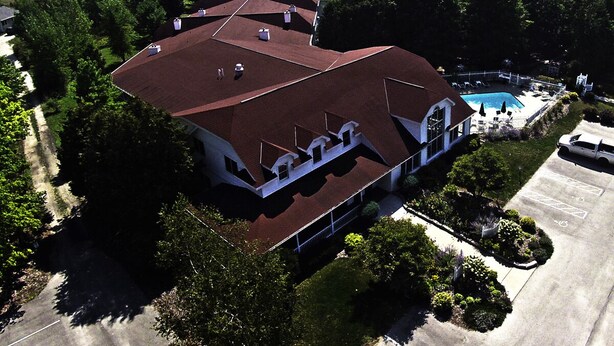 A large building with multiple roofs, a swimming pool, and a parking area.
