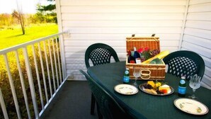 A table set for two on a balcony with a wicker basket containing food and drinks.
