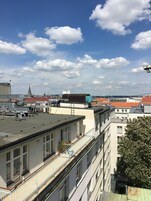 Un edificio de varios pisos con balcones, cielo despejado y una torre distante en la lejanía.