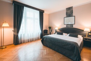 Quarto de hotel com uma cama grande, duas mesas de cabeceira com luminárias, uma cadeira, uma pequena mesa com um vaso de flores e uma decoração de parede com padrão de zebra.