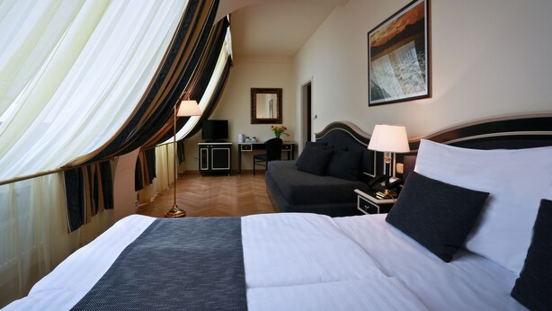 A hotel room with a large bed, a desk, a chair, and a sofa. - Hotel Elysee (Prague)
