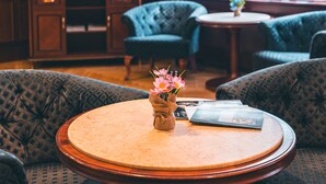 A cozy room with patterned blue sofas, a round wooden table with a vase of flowers, and a television in the background. - Hotel Elysee (Prague)
