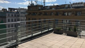 A rooftop terrace with a glass balustrade, tiled flooring, and potted plants. - Hotel Elysee (Prague)