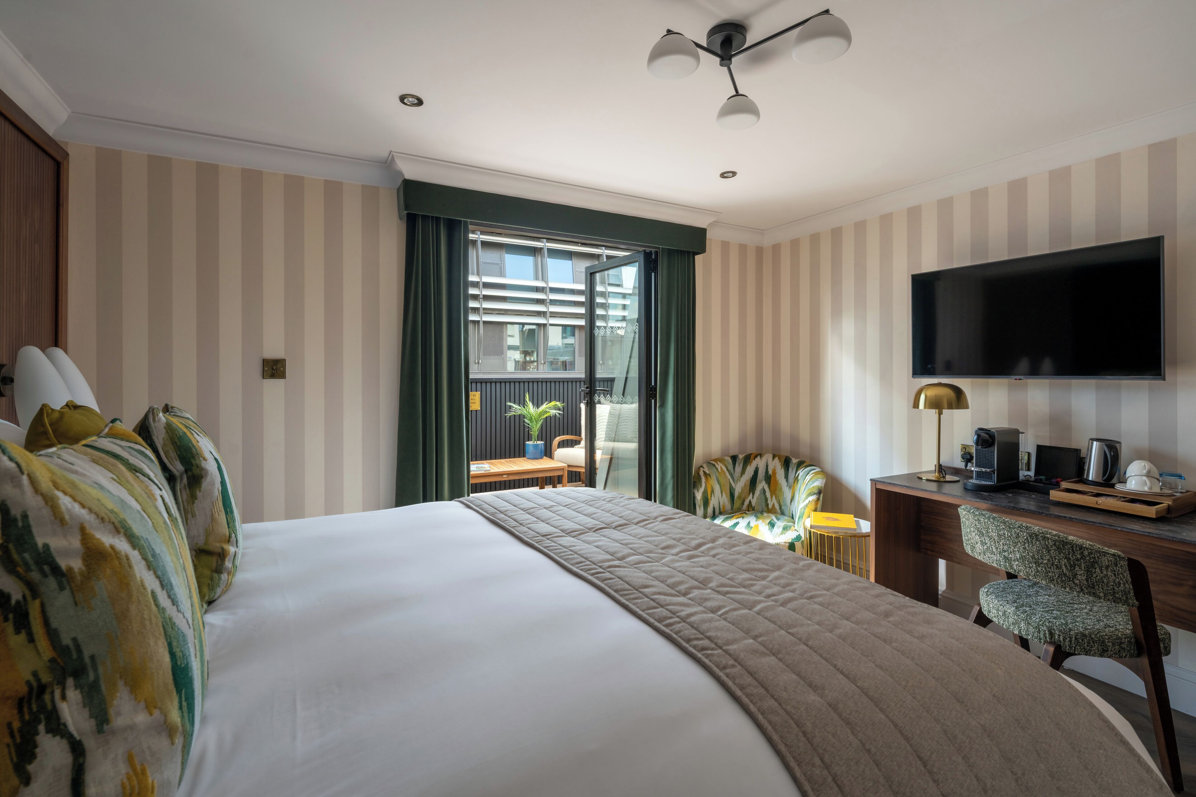 Habitación de hotel con una cama grande, un escritorio con computadora, un televisor de pantalla plana y un balcón con vistas.