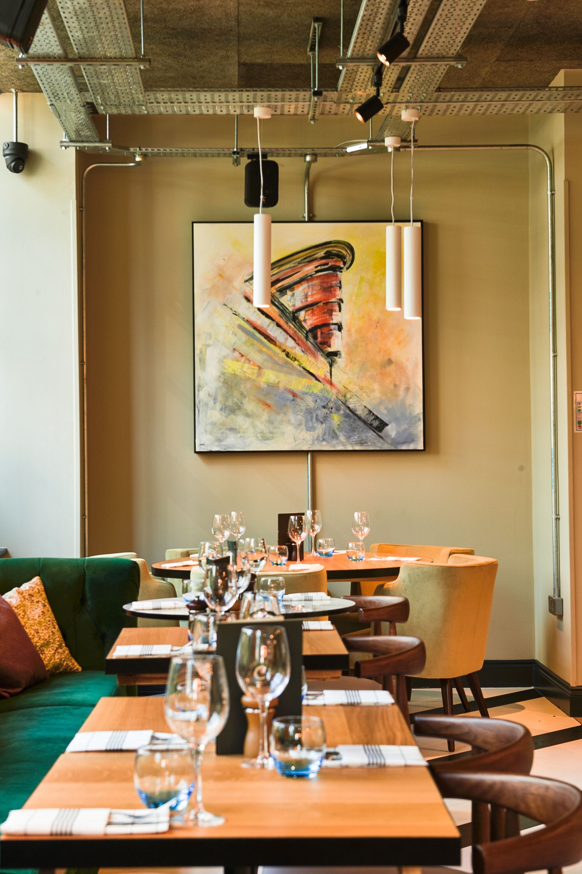 Un restaurante con mesas dispuestas para comer, un sofá verde y un cuadro abstracto grande en la pared.